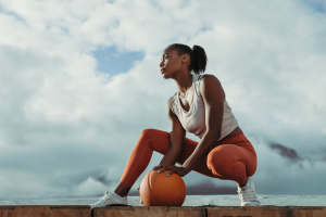 Fit woman wearing sportswear with basketball taking break from workout on rooftop. Female athlete sitting on rooftop relaxing after exercise.