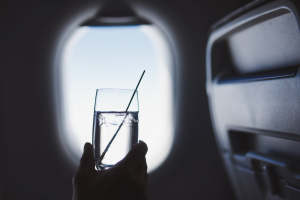 Passenger enjoy drink during flight. Man holding glass of gin and tonic against airplane window.