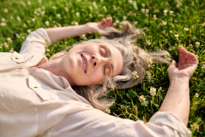 Wonderful time. Adult gray-haired smiling woman with drooping eyelids lying on flowering grass on fine day